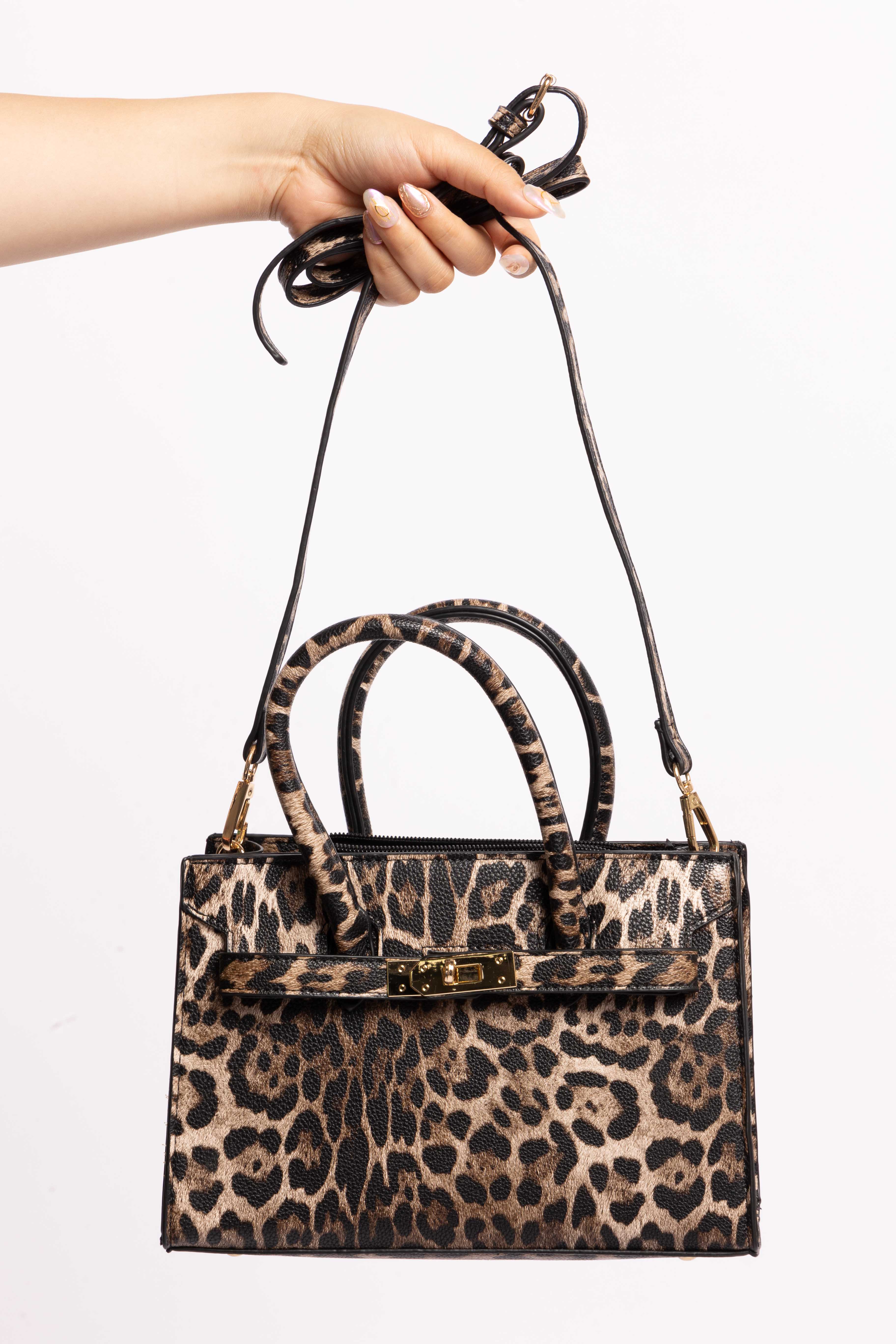 Leopard print handbag with a detachable shoulder strap and gold accents, held by hand.