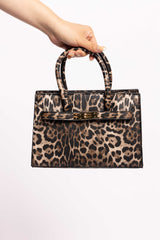 Leopard print handbag with dual top handles and a gold lock, held by hand.