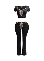 Front view of black two-piece set with nude trim, featuring a scoop-neck crop top and high-waisted flared pants.